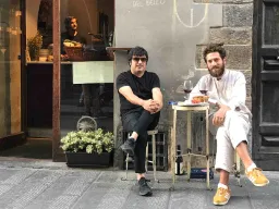 Två män njuter av ett glas vin vid ett litet bord på gatan Två män njuter av ett glas vin vid ett litet bord på gatan