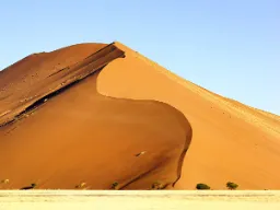 En av Sossusvleis ikoniska röda sanddyner reser sig majestätiskt mot den klara himlen