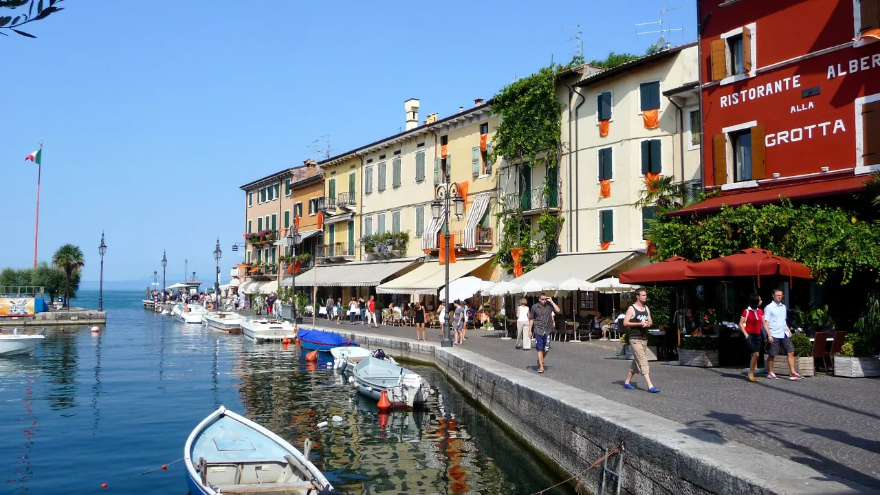 Hamnen i Lazise vid Gardasjön med båtar, strandpromenad och historiska byggnader längs vattnet Hamnen i Lazise vid Gardasjön med båtar, strandpromenad och historiska byggnader längs vattnet